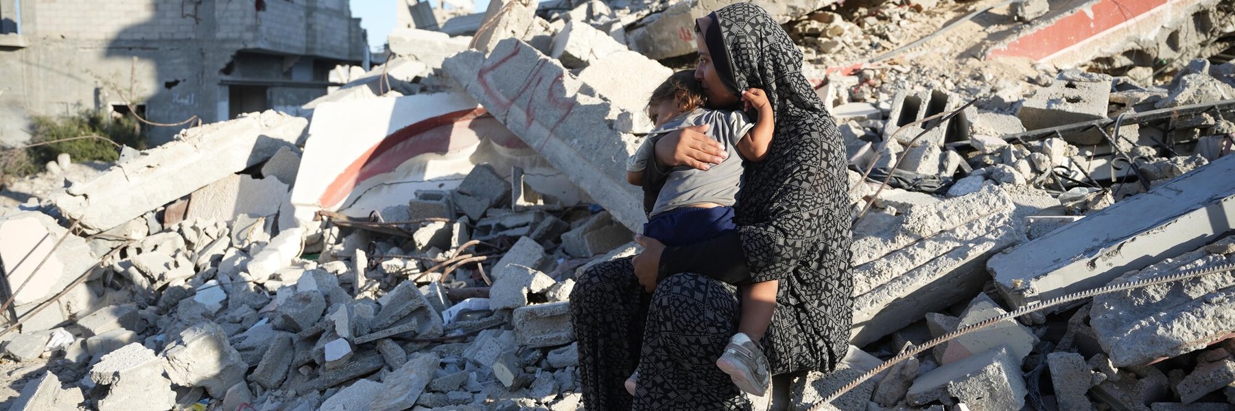 A woman holds her child sitting on rubble in Gaza.