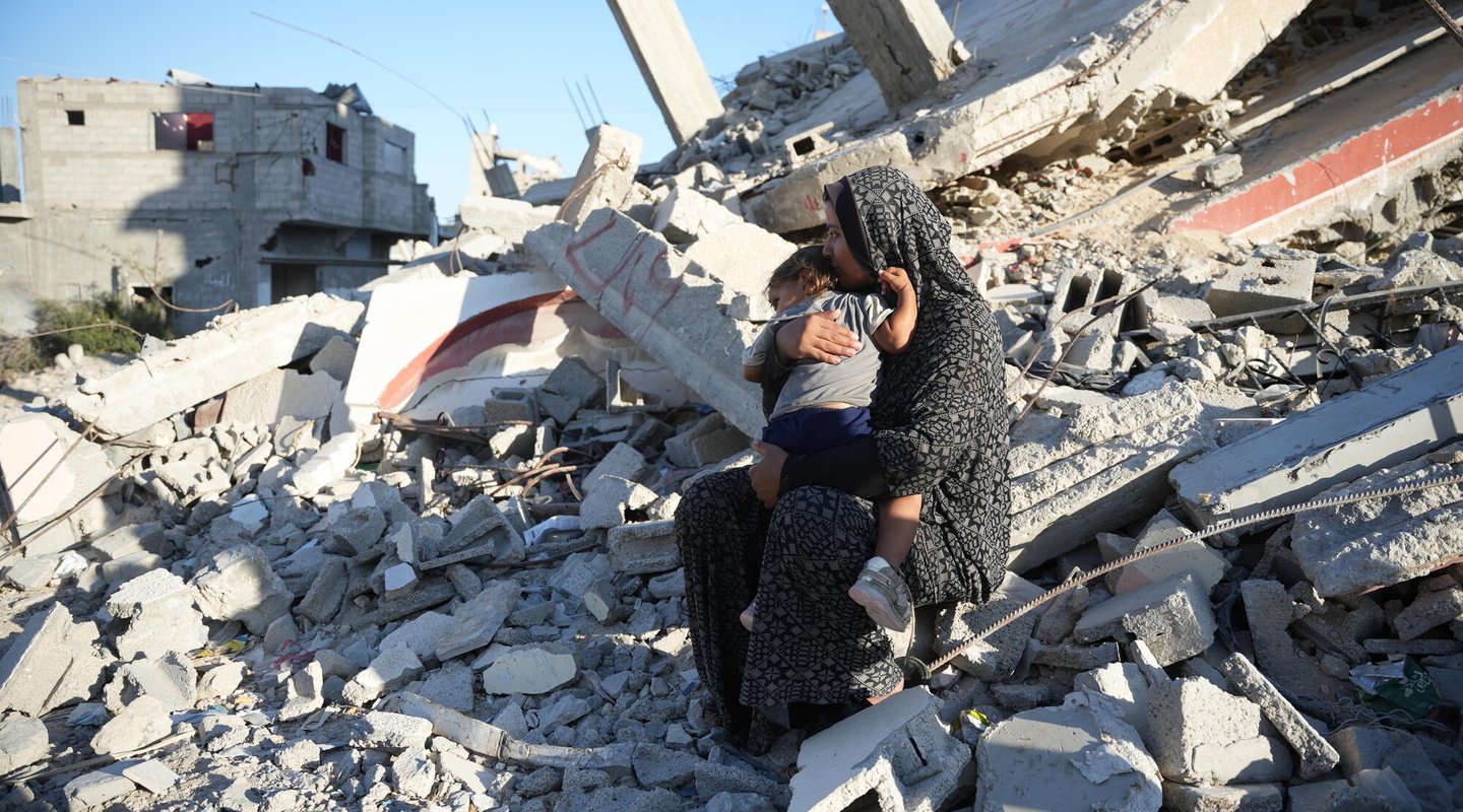 A woman holds her child sitting on rubble in Gaza.