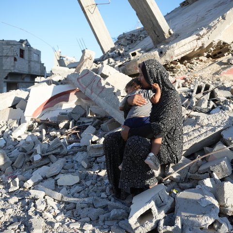 A woman holds her child sitting on rubble in Gaza.