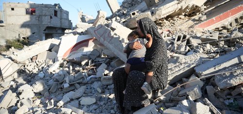 A woman holds her child sitting on rubble in Gaza.