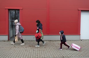 Julia and her children walk with luggage past a red painted wall