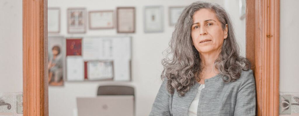 Hero Anwar of REACH leaning against a wooden door frame to her office with arms folded looking into the camera.