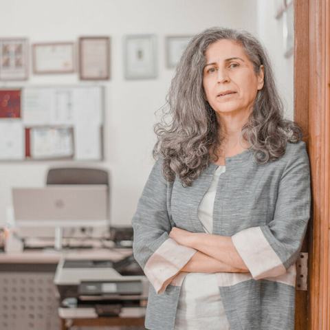 Hero Anwar of REACH leaning against a wooden door frame to her office with arms folded looking into the camera.