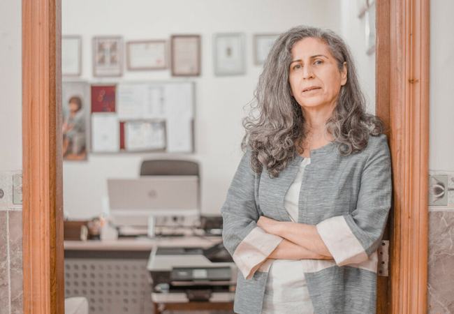 Hero Anwar of REACH leaning against a wooden door frame to her office with arms folded looking into the camera.