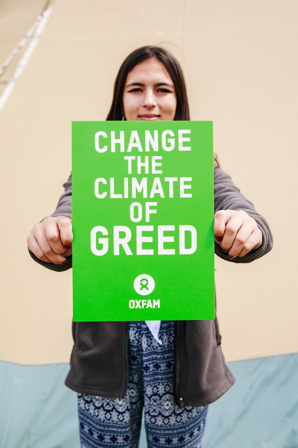 19-year-old British-Bangladeshi Mya-Rose who has long straight hair holds a green sign to the camera that says 'change the climate of greed'