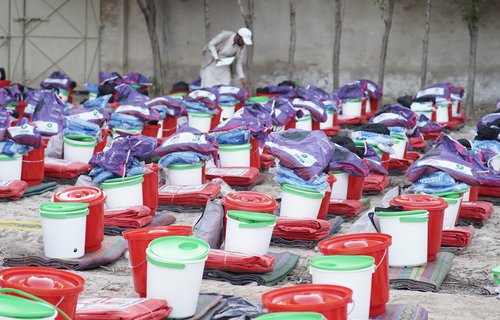 Tameer e Khalaq Foundation worker Ashraf inspecting rows of emergency kits including buckets and blankets.