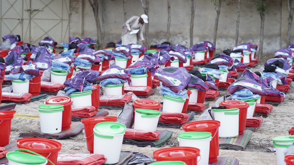Tameer e Khalaq Foundation worker Ashraf inspecting rows of emergency kits including buckets and blankets.