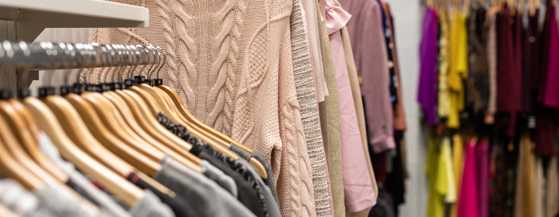 Pastel knitted jumpers hanging on racks in a large shop.