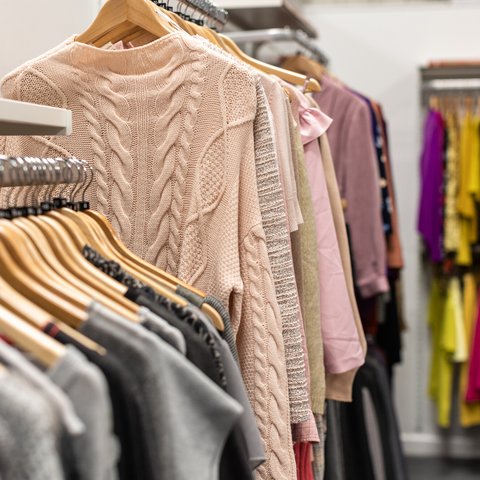 Pastel knitted jumpers hanging on racks in a large shop.