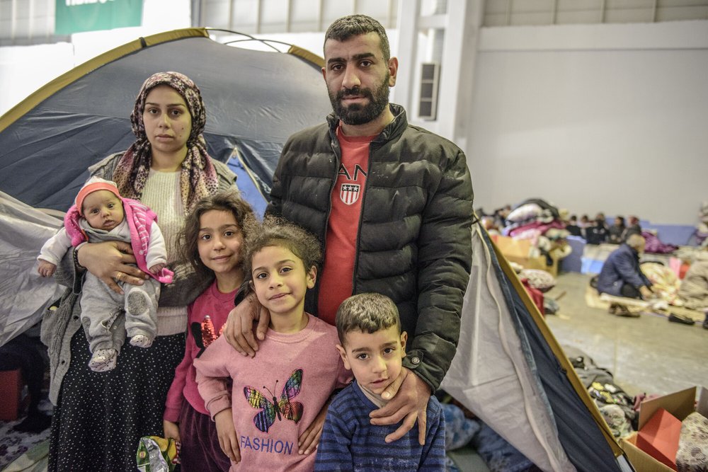 A family in front of a tent in a public shelter following an earthquake.