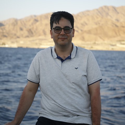 Wassem in his 40s sits with a view of the water and mountains behind him.