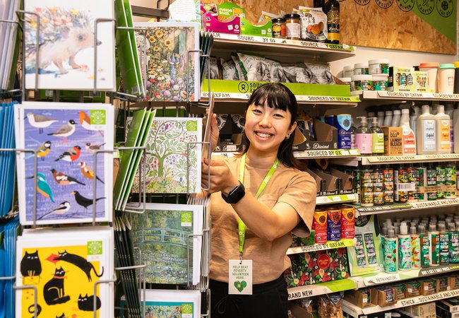 Volunteer Mahiro smiling in the Islington Oxfam Shop during her volunteer shift.