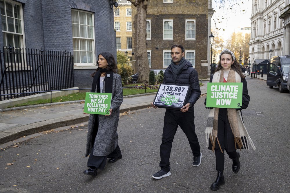 Three people walking down the street with signs that say 'climate justice now' and 'together we say polluters must pay'