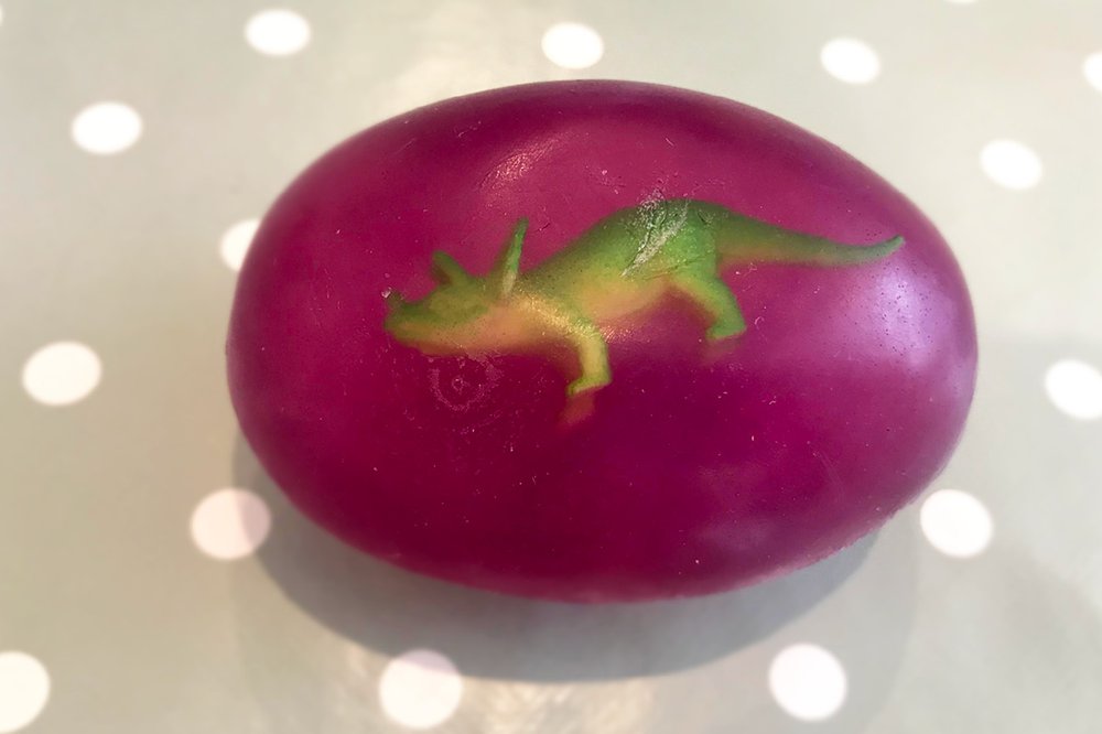A plastic dinosaur suspended inside an egg-shaped homemade soap