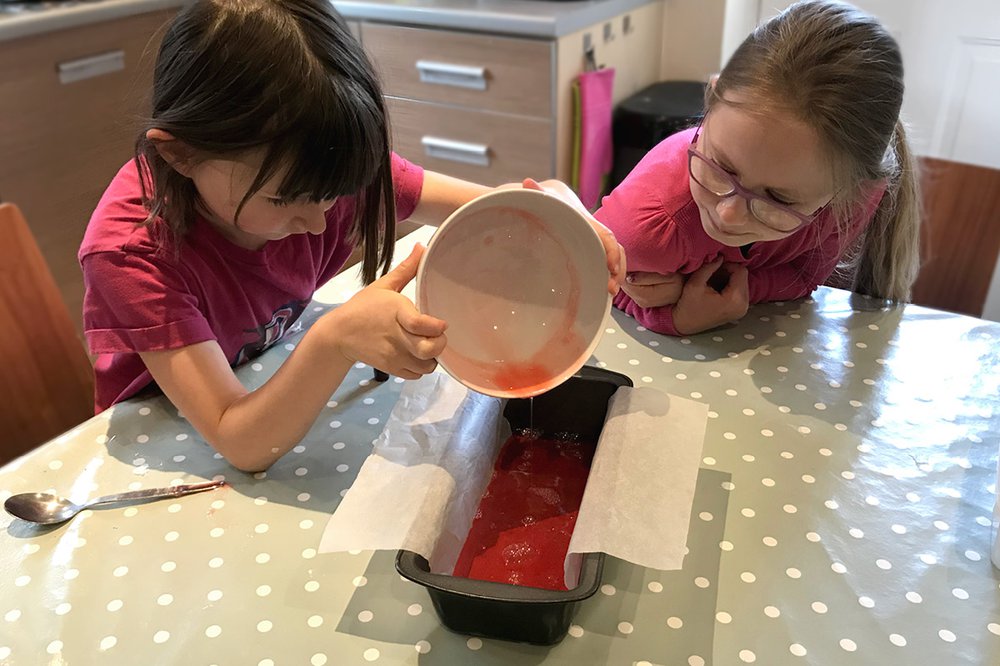 Two children look at a bowl of red liquid soap ingredients