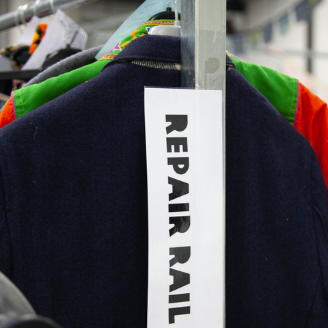 A clothes rail with a sign stuck to the front that says 'repair rail'