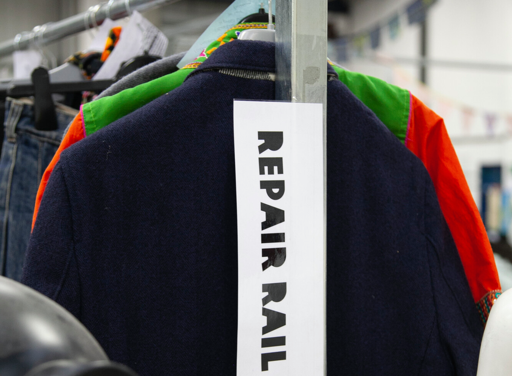 A clothes rail with a sign stuck to the front that says 'repair rail'
