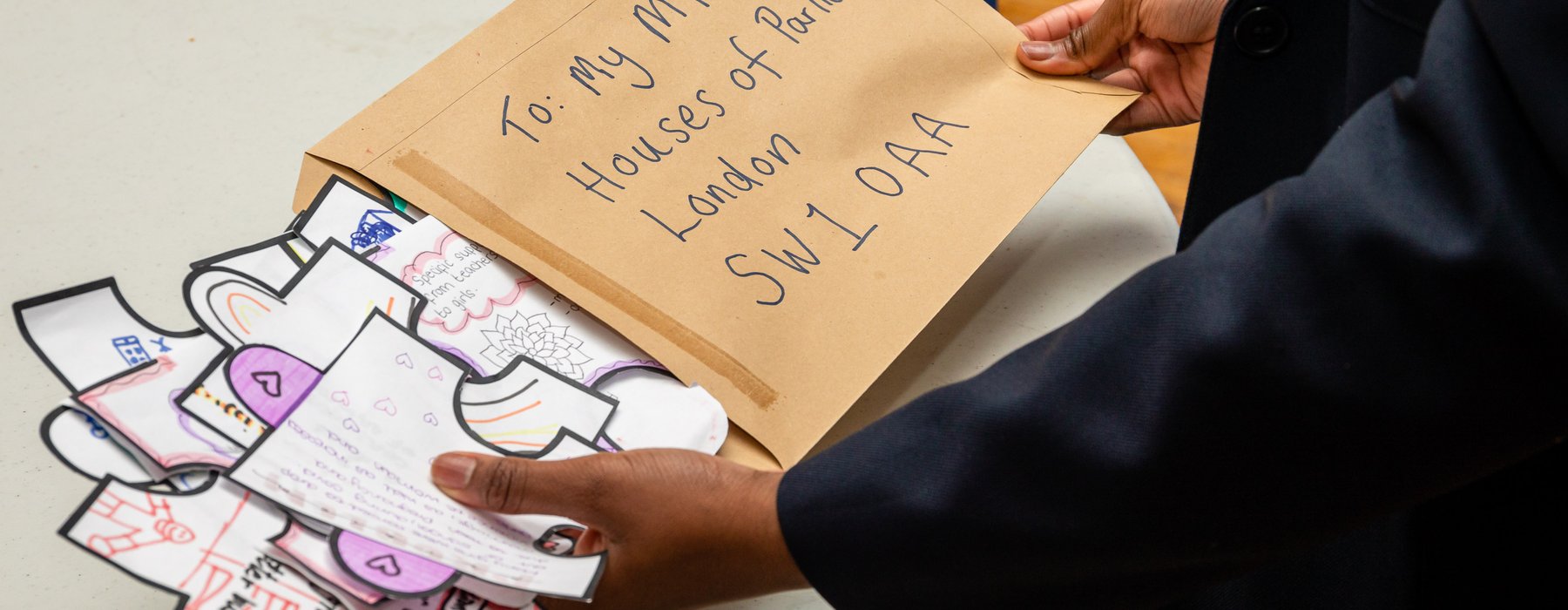 A brown envelope with: To: My Mp, Houses of Parliament, London, SW1 OAA is backed with drawings and writing on paper in the shape of giant puzzle pieces by a child.