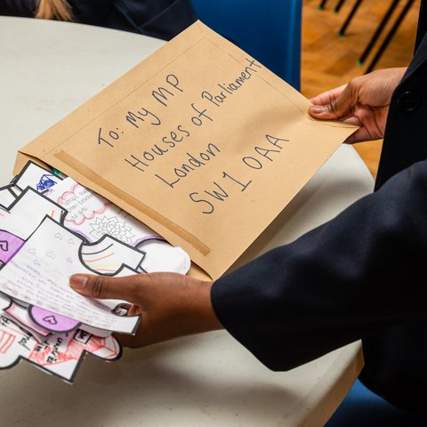 A brown envelope with: To: My Mp, Houses of Parliament, London, SW1 OAA is backed with drawings and writing on paper in the shape of giant puzzle pieces by a child.