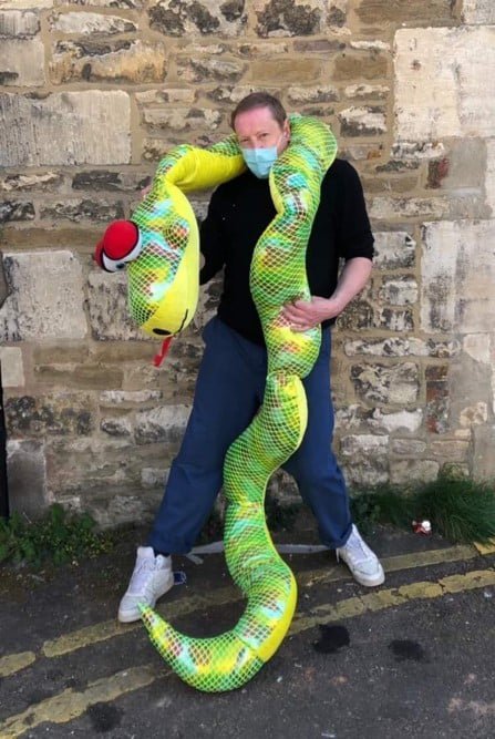 Shop staff member David with a giganitic green plush toy snake wrapped around him