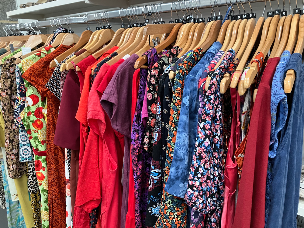 A row of summer dresses hang on a rail in a shop in a big warehouse
