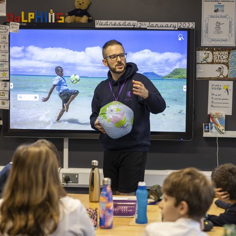 A teacher holds a globe as he stands at the front of the call at Valley Invicta Primary School at King's Hill