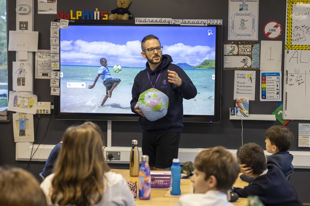 A teacher holds a globe as he stands at the front of the call at Valley Invicta Primary School at King's Hill