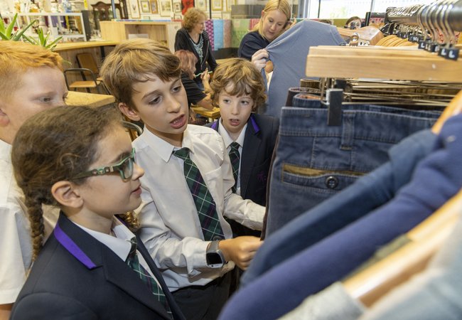 Four children in school uniform look at a rack of second hand jeans.