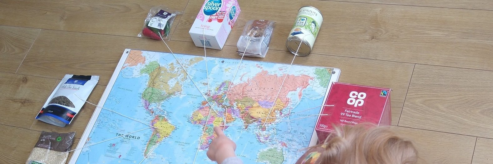 A child looks at a map of the world with pins that strings to bags of real food from their family cupboard