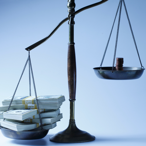 Set of scales with heavy bank notes on the left and small stack of light coins on the right.