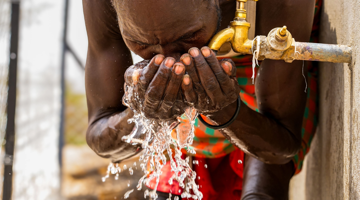 Man gathering water in his hands from a tap and drinking it, with water splashing over the sides of his hands.