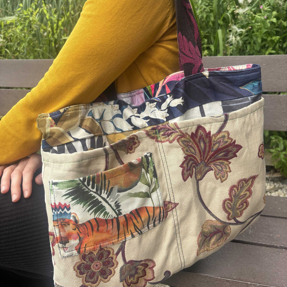 A person in a yellow cardie sat on a park bench with a colourful Loom bag over their shoulder.