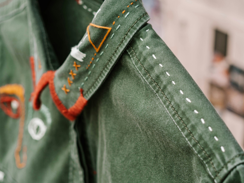 Close up of a green shirt with white and orange thread added as detail.