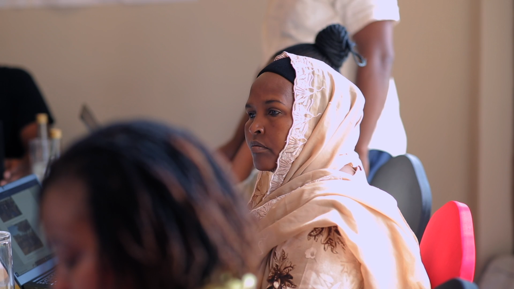 A Woman in cream-coloured lace-edged hijab sits at a table for a workshop.