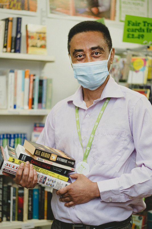 Volunteer Wagayu is wearing a face mask and poses in an Oxfam shop