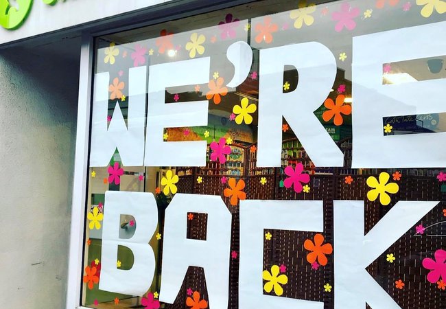 An Oxfam shop window with the words 'We're back' in white paper letters on it