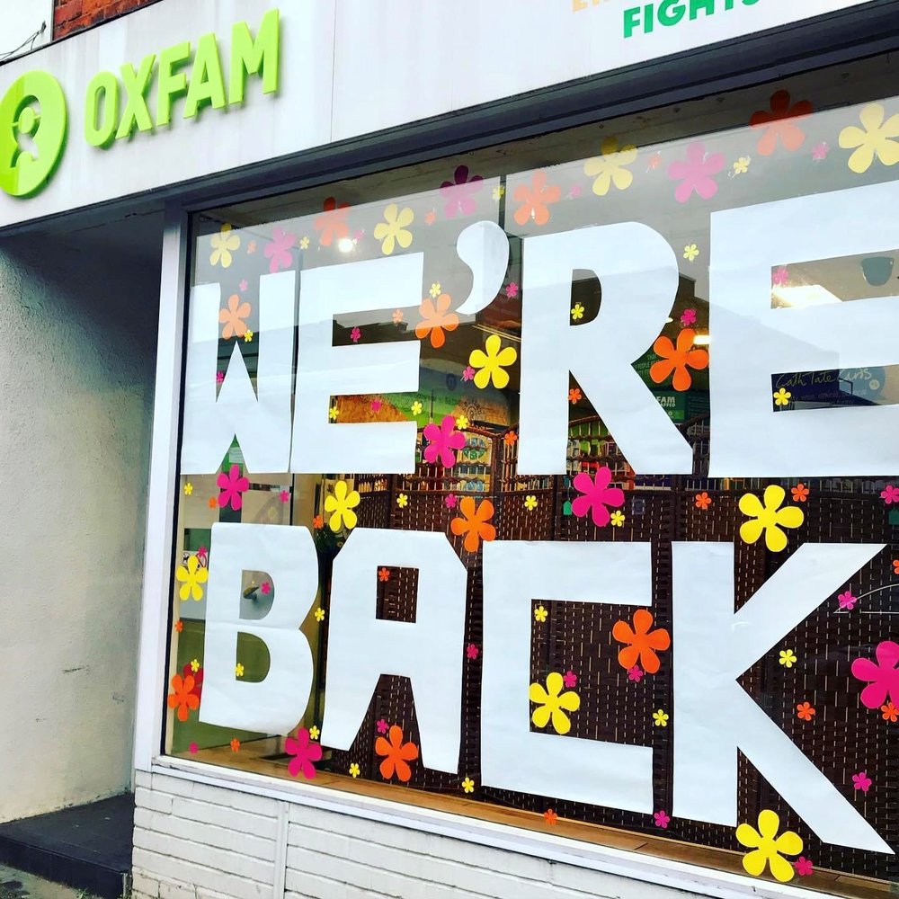 An Oxfam shop window with the words 'We're back' in white paper letters on it
