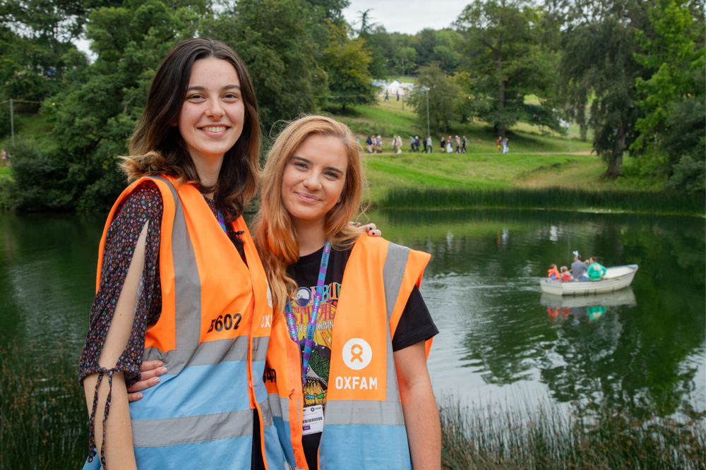 Two Oxfam Festival Stewards standing in front of a lake at a festival