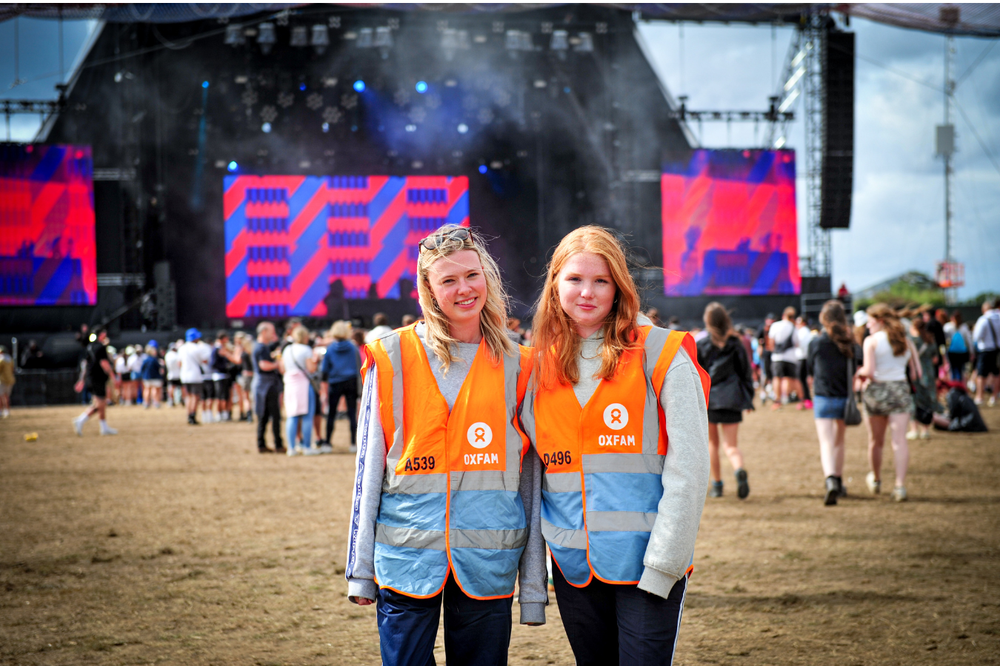 Two Oxfam festival volunteers standing in front of the Reading Festival main stage