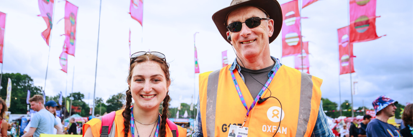 Two Oxfam Festivla Volunteers smiling with festival flags in the background