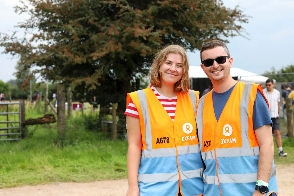 Two Oxfam festival volunteers working on an entrance gate and smiling at the camera