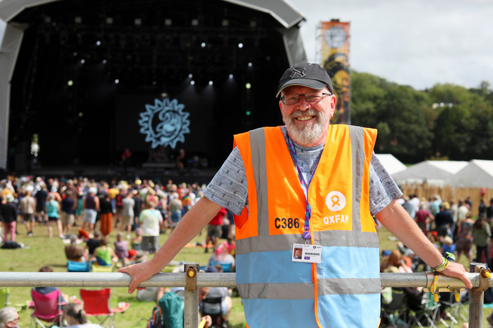 Oxfam festival steward smiling at the camera on an accessibility platform with the main stage in the background
