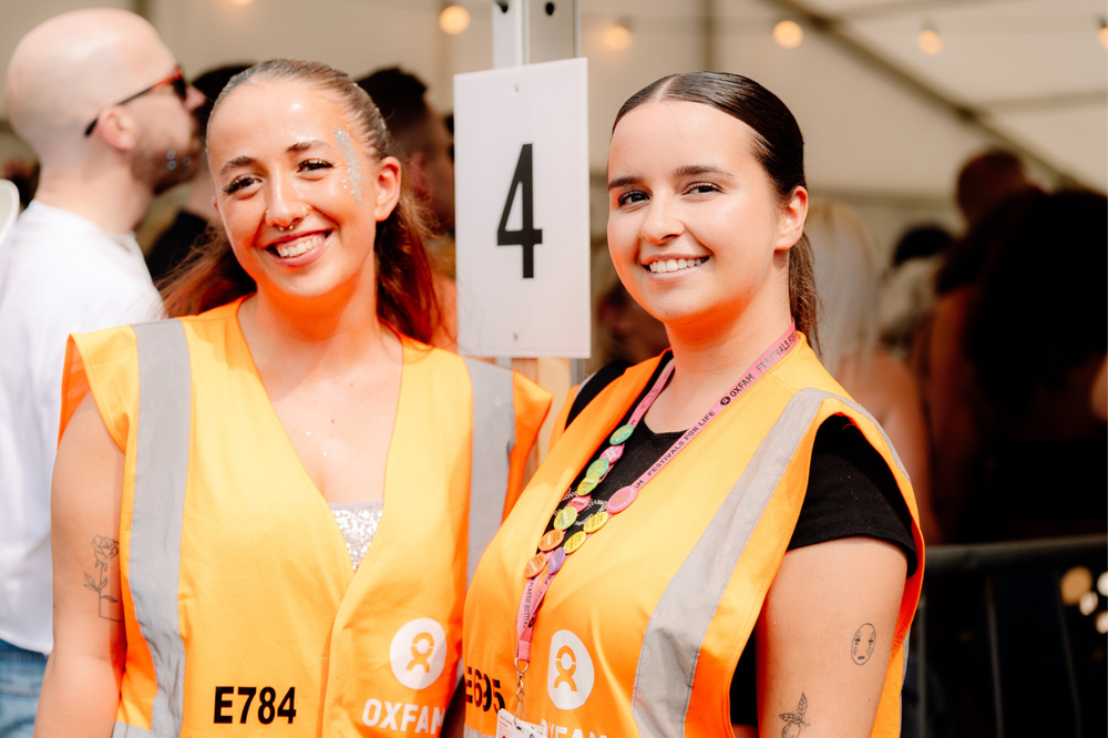Two smiling Oxfam festival stewards volunteering ona festival gate