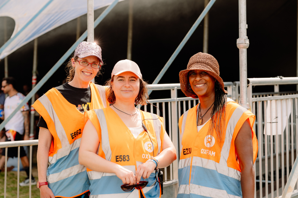 Three smiling Oxfam Festival volunteers standing outside a festival venue