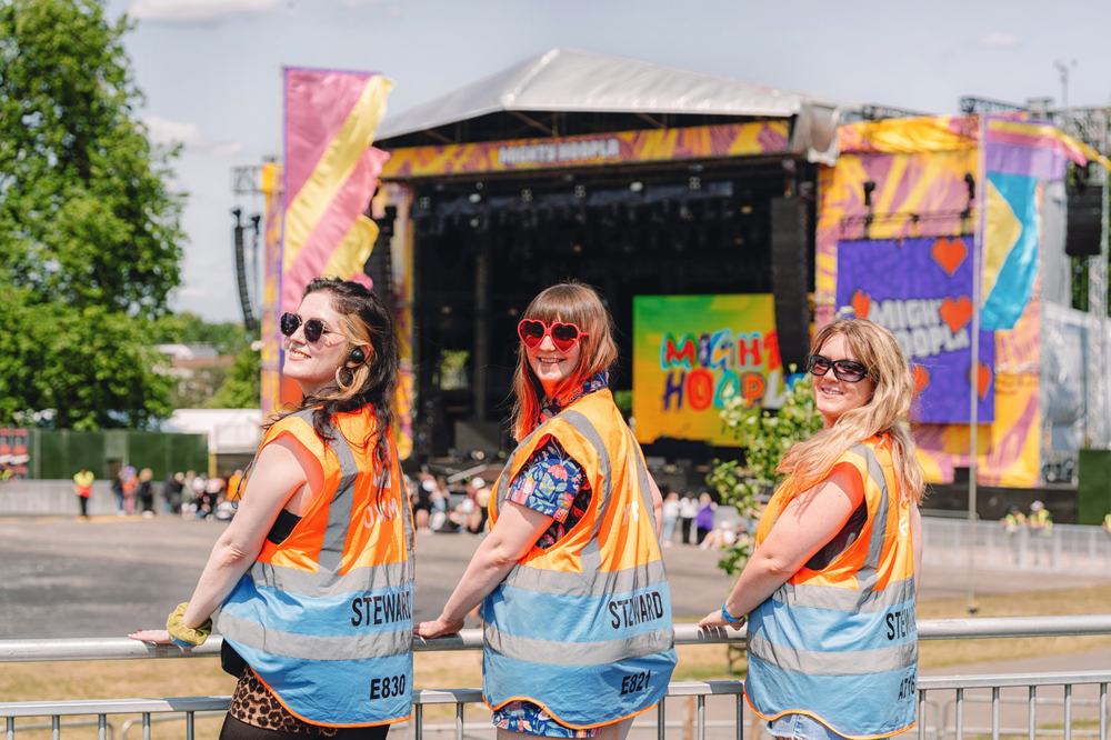 3 Oxfam festival stewards working on an accessibility platform with Mighty Hoopla's main stage in the backgroud