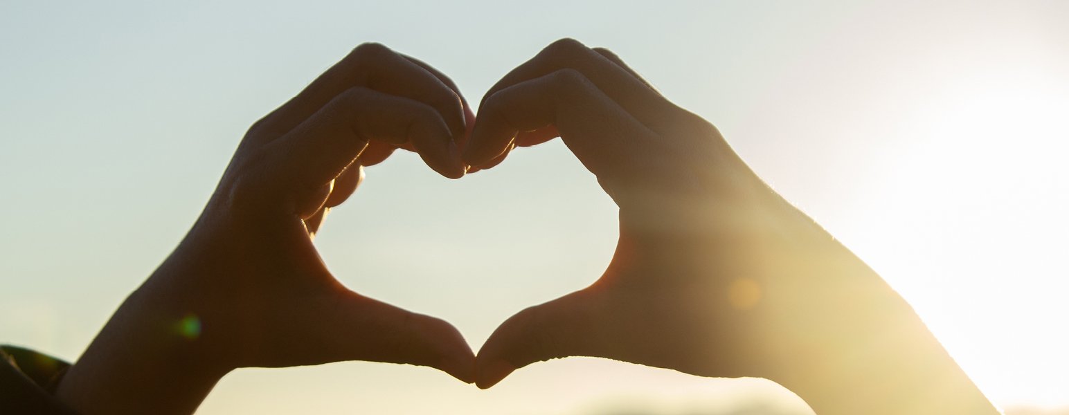 Two hands making a heart shape, with the sun behind