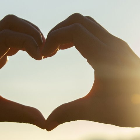 Two hands making a heart shape, with the sun behind