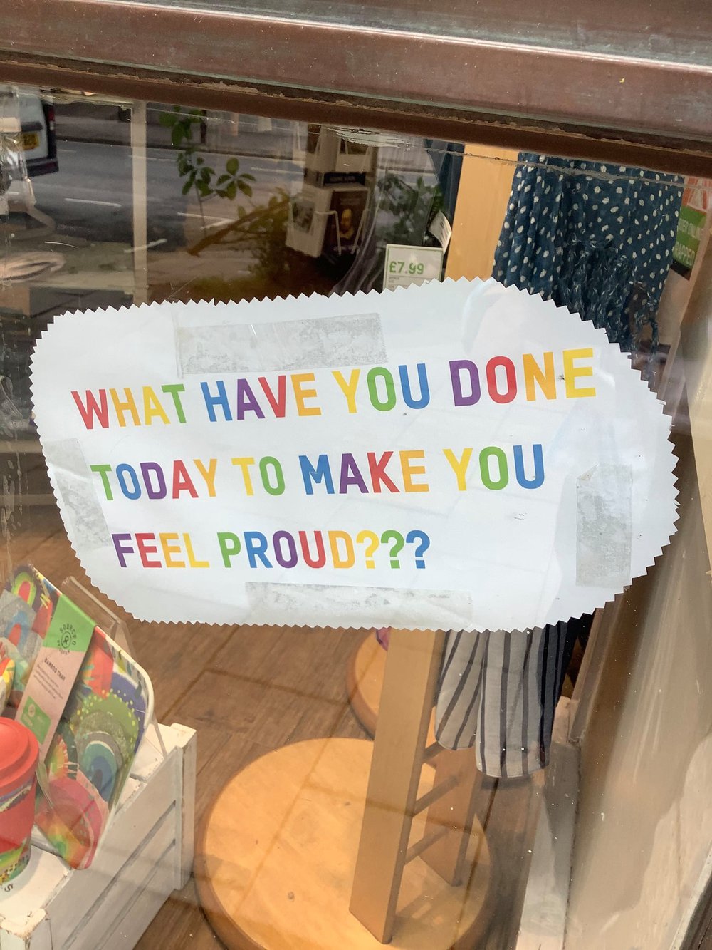 An Oxfam shop window with the words in rainbow colours 'what have you done today to make you feel proud'