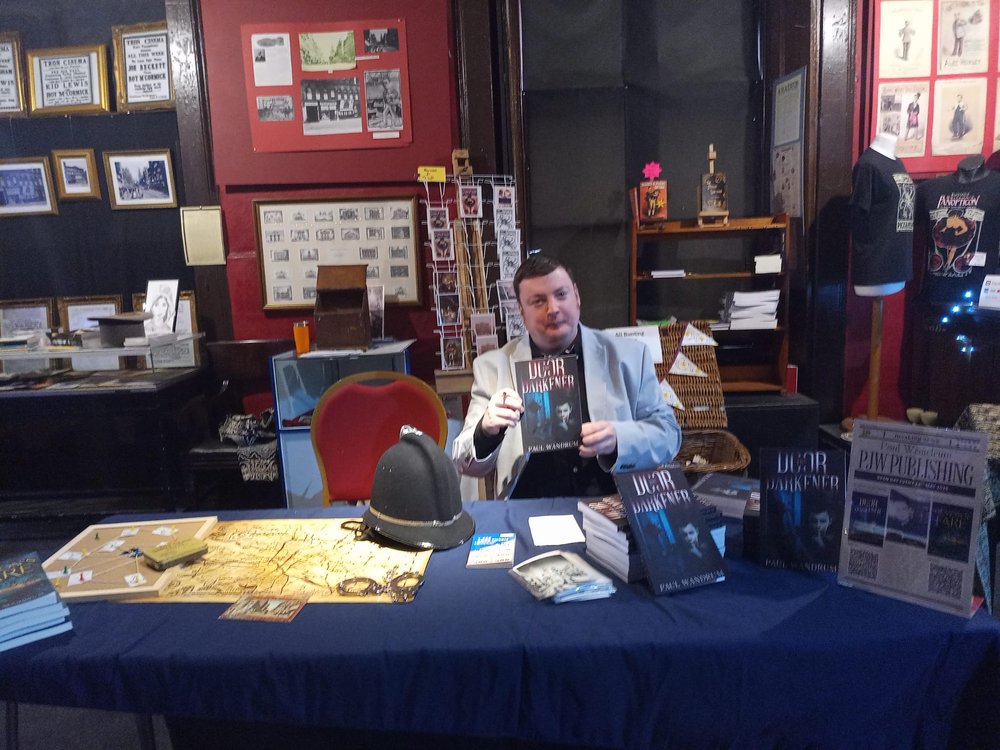 Paul sitting behind a book signing table, holding a copy of his book
