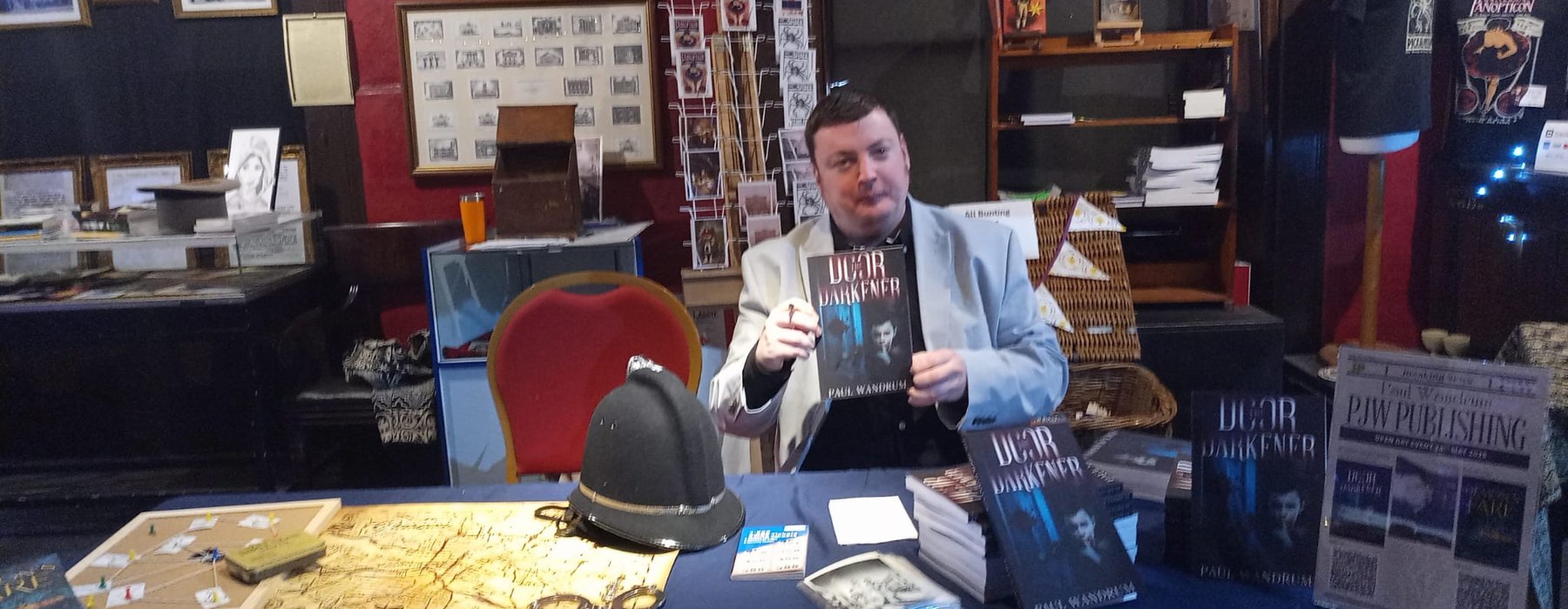 Paul sitting behind a book signing table, holding a copy of his book
